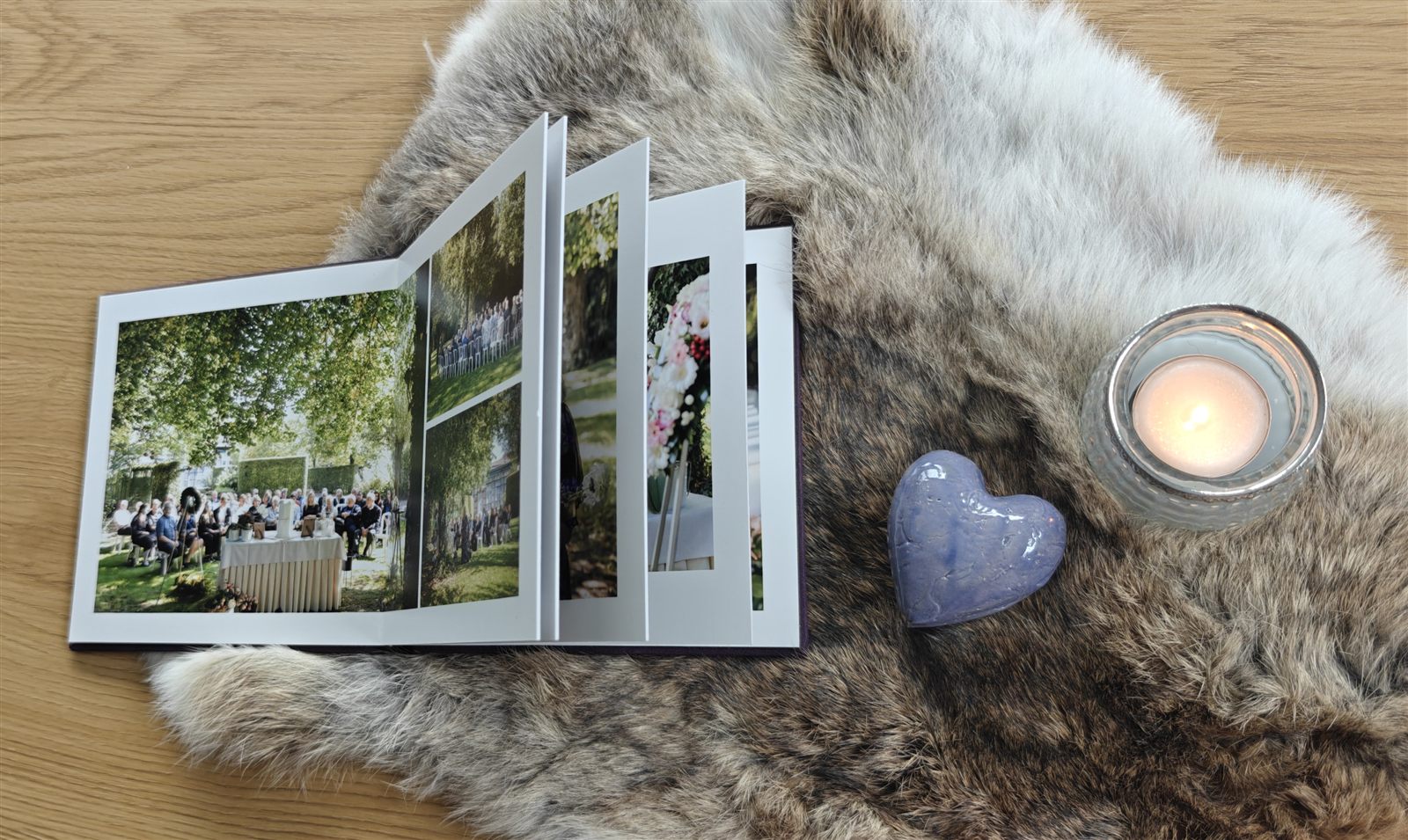 Een opengeslagen fotoalbum van een afscheid op een vacht, naast een keramieken hartje en een brandende kaars