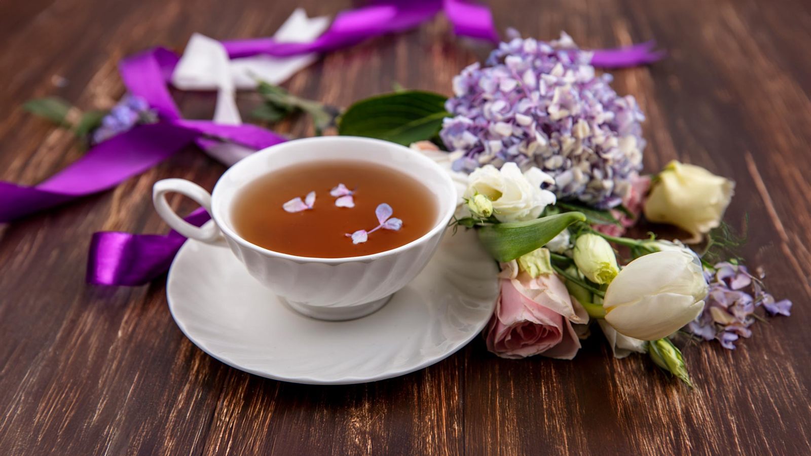 Een kopje thee op een houten tafel, naast een boeket bloemen en een paars lint